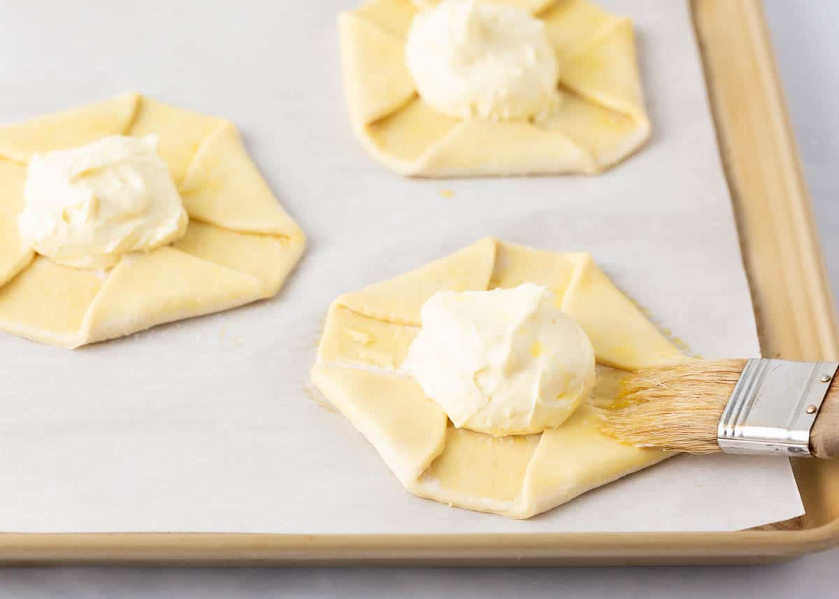 Brushing cheese danish with egg wash.