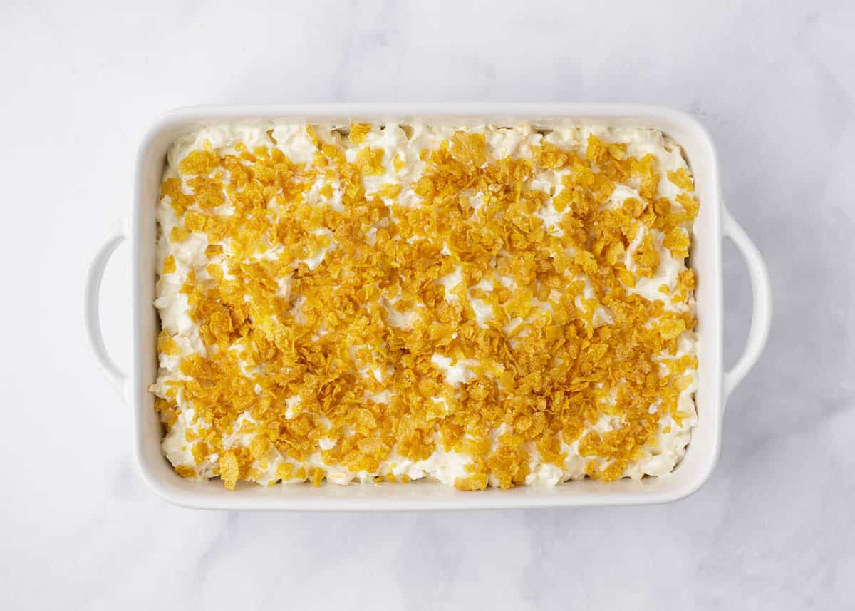 Unbaked funeral potatoes recipe with cornflake topping in a white baking dish.