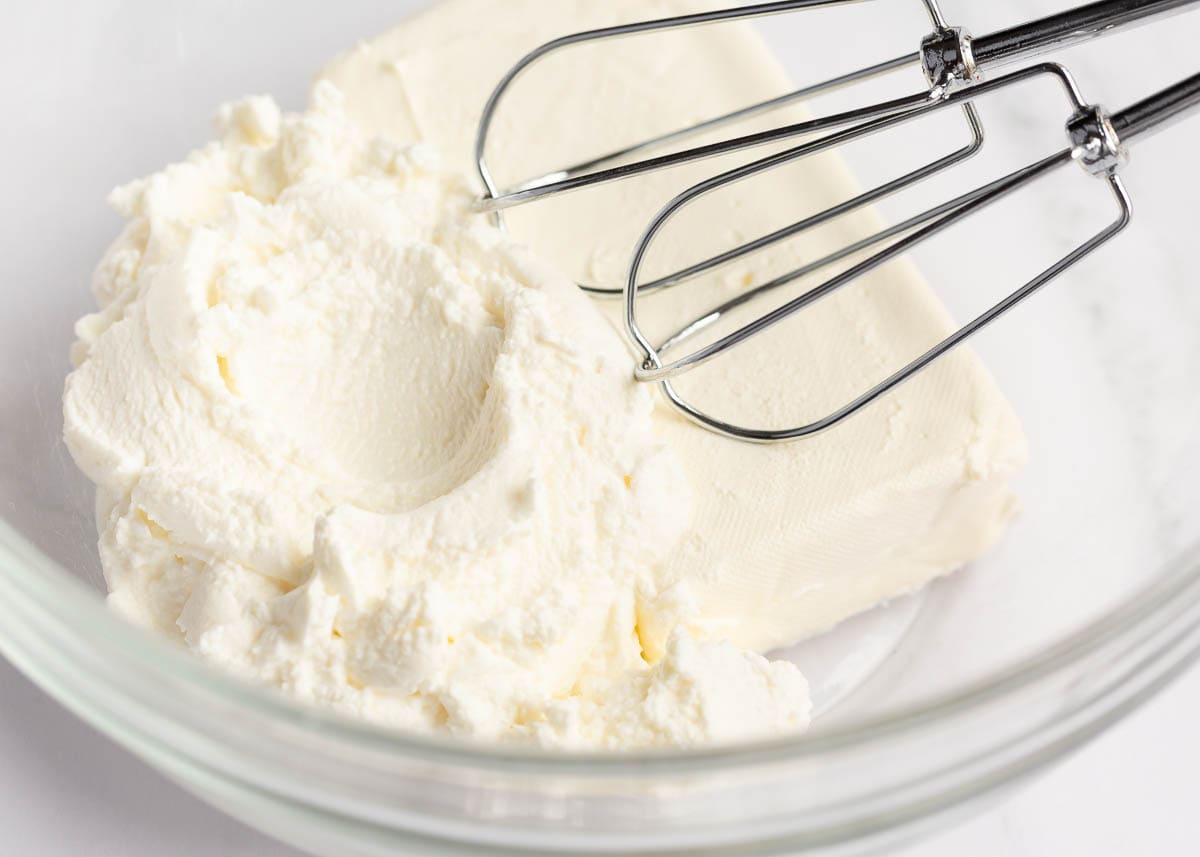 Cream cheese and ricotta in a glass bowl with mixing beaters.