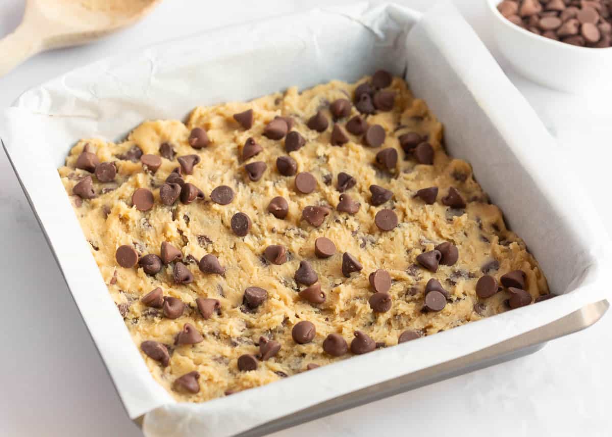 Chocolate chip cookie bar batter in a parchment lined baking pan.