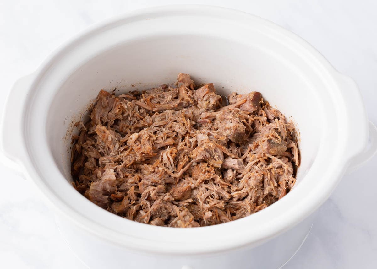 Shredded pork in a white crockpot.