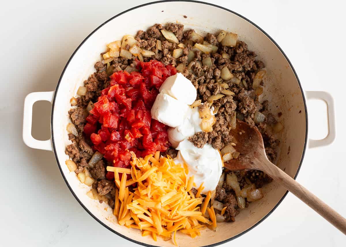 Adding cream cheese, cheese and tomatoes to ground beef in a skillet.