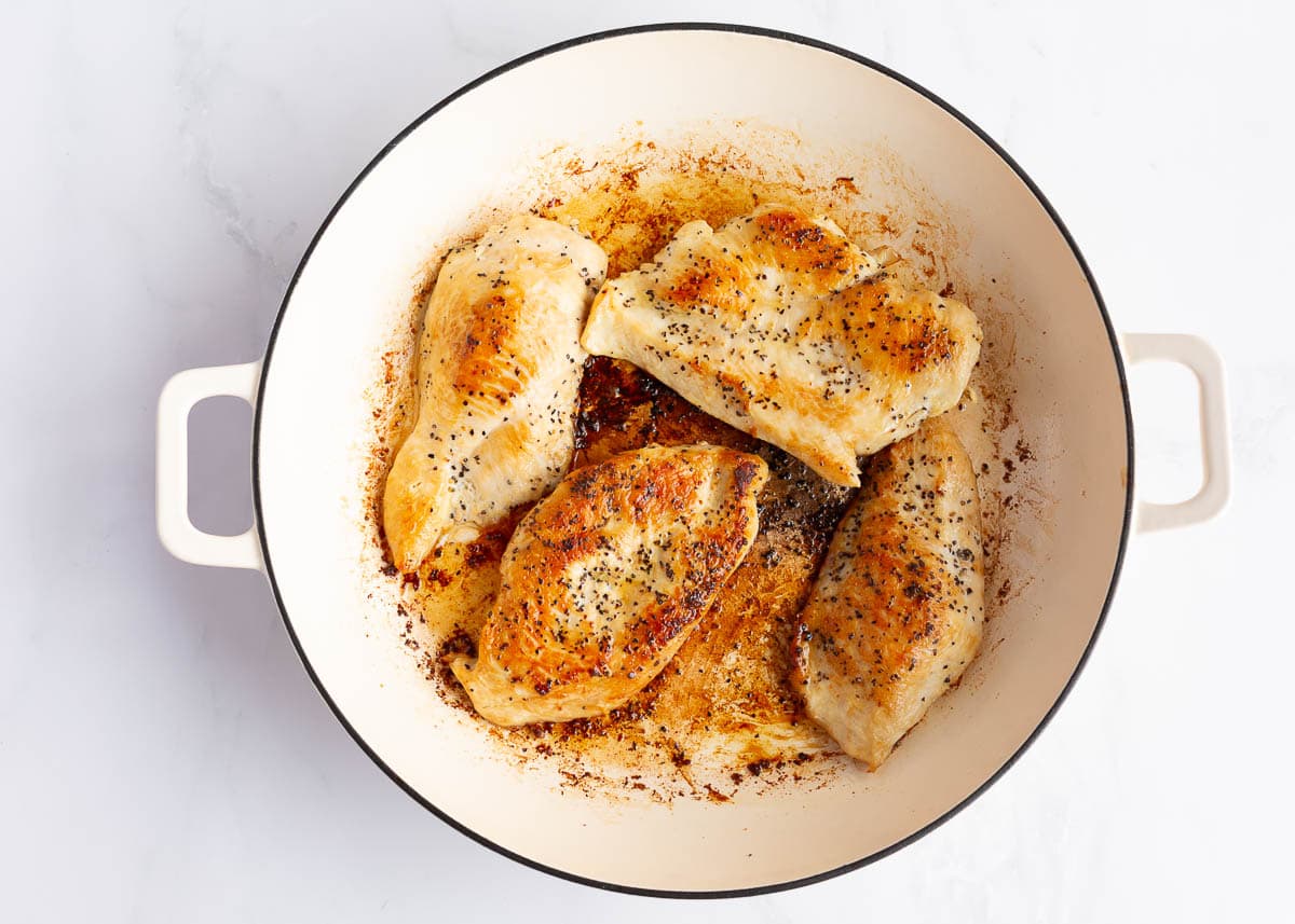 Seared chicken in large white skillet.