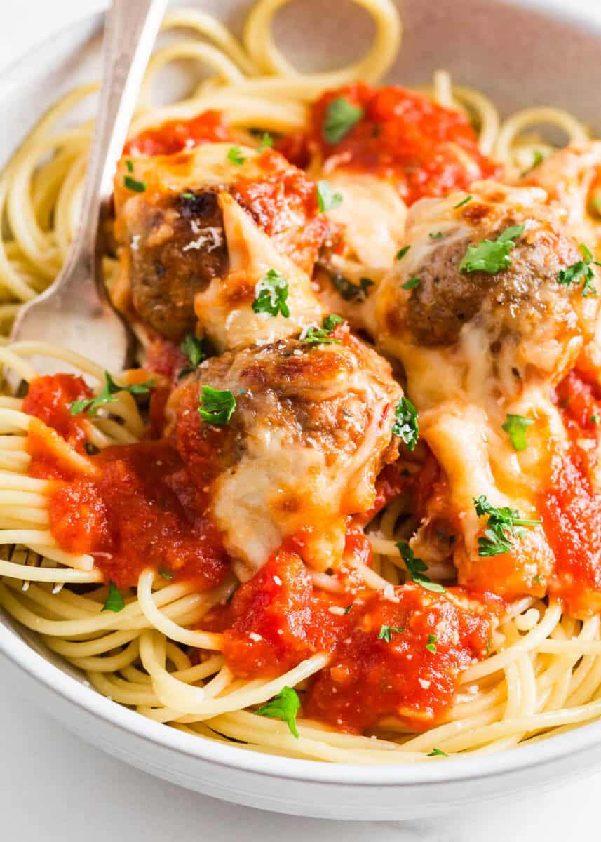 Chicken Parmesan meatballs served in a bowl with spaghetti noodles.