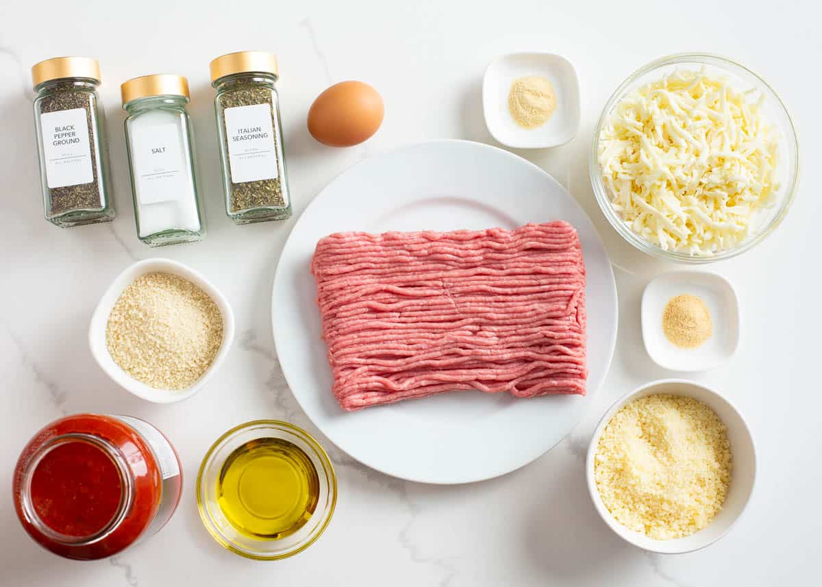 Ground chicken, parmesan, mozzarella, salt, pepper, Italian seasoning, egg, marinara sauce and Panko on counter.