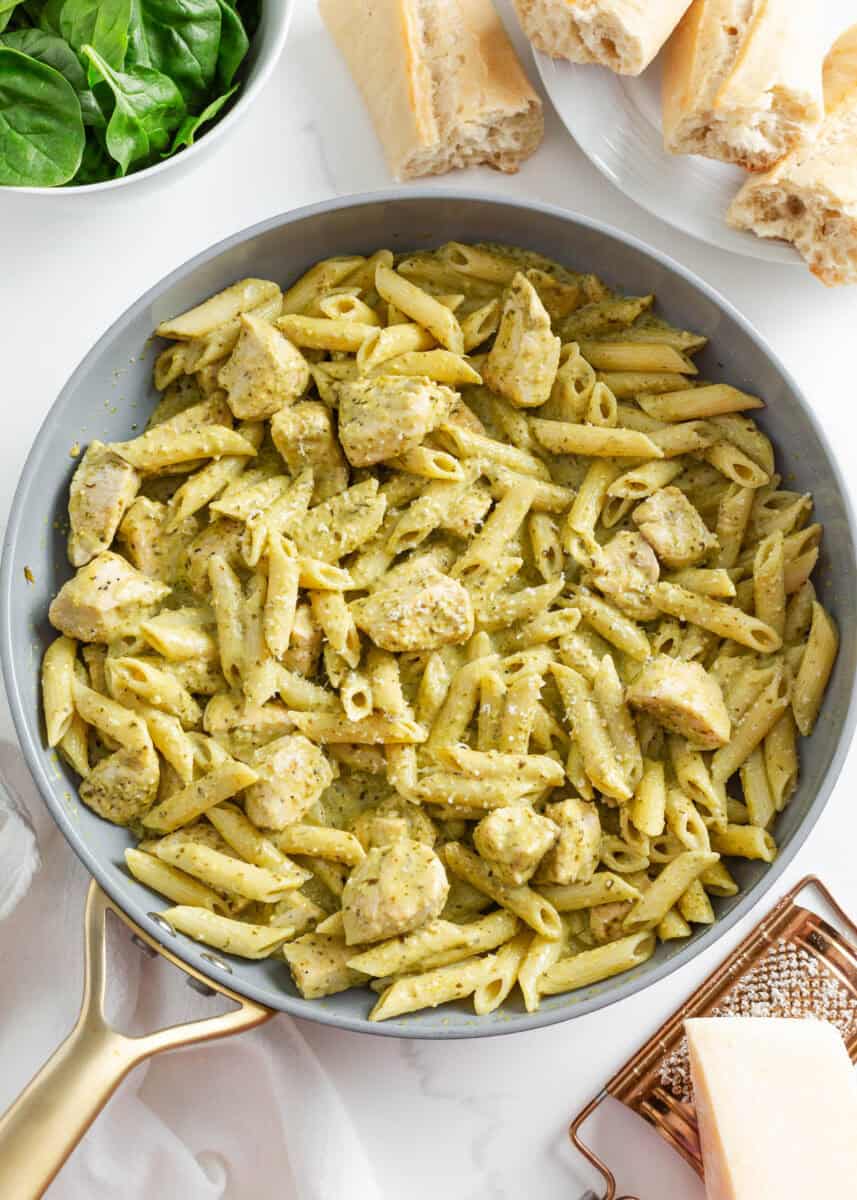 Chicken combined with pesto sauce in a skillet.