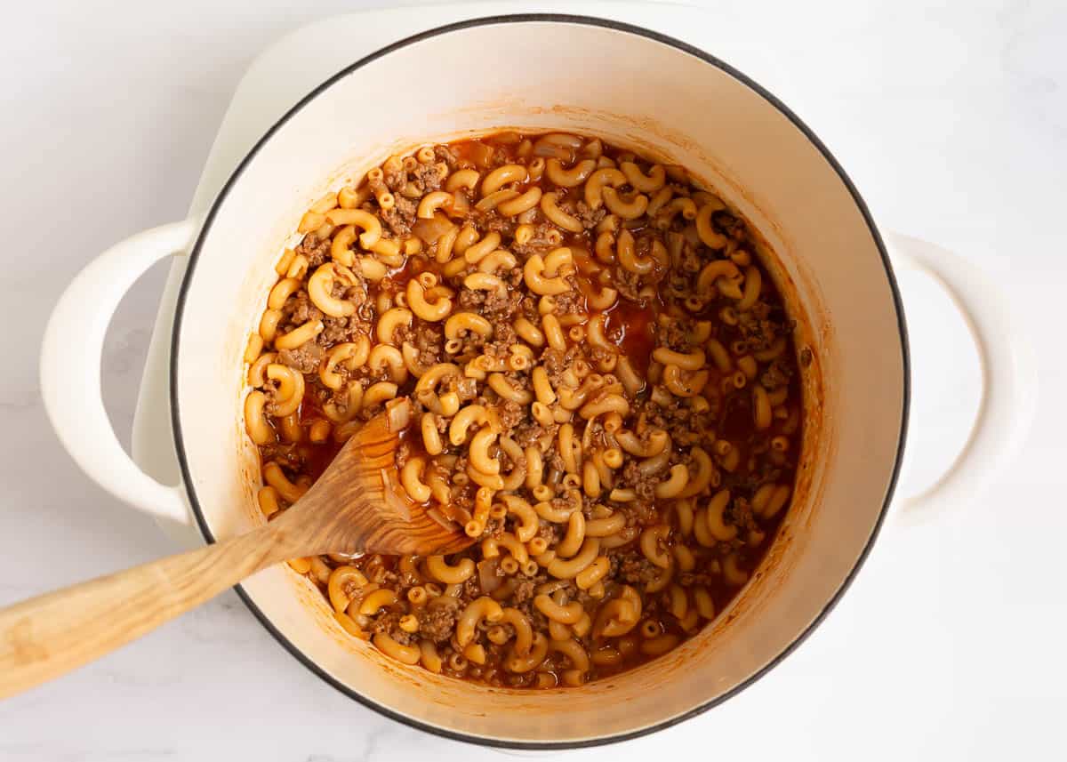 Dry noodles with ground beef, tomato paste and broth in a pot.