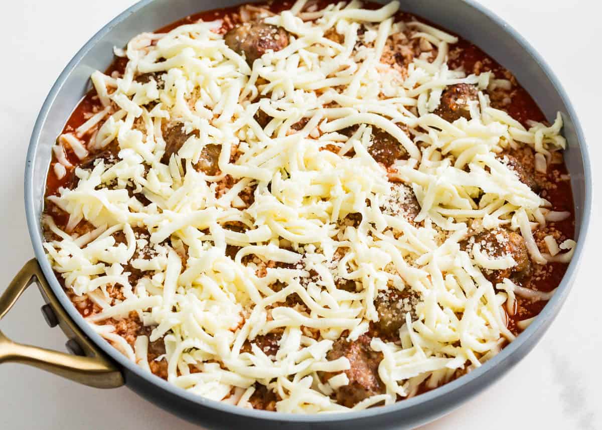 Cheese covering meatballs in a skillet.