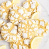 Lemon crinkle cookies on parchment covered cooling rack with fresh lemon slices.