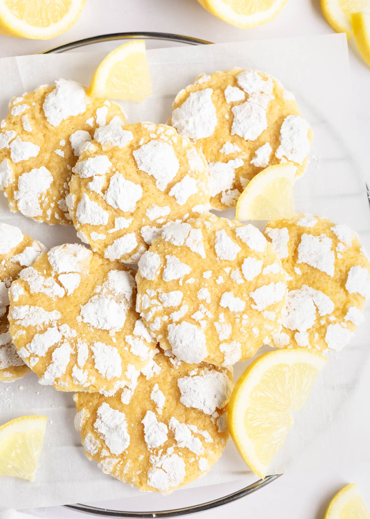 Lemon crinkle cookies on parchment covered cooling rack with fresh lemon slices.