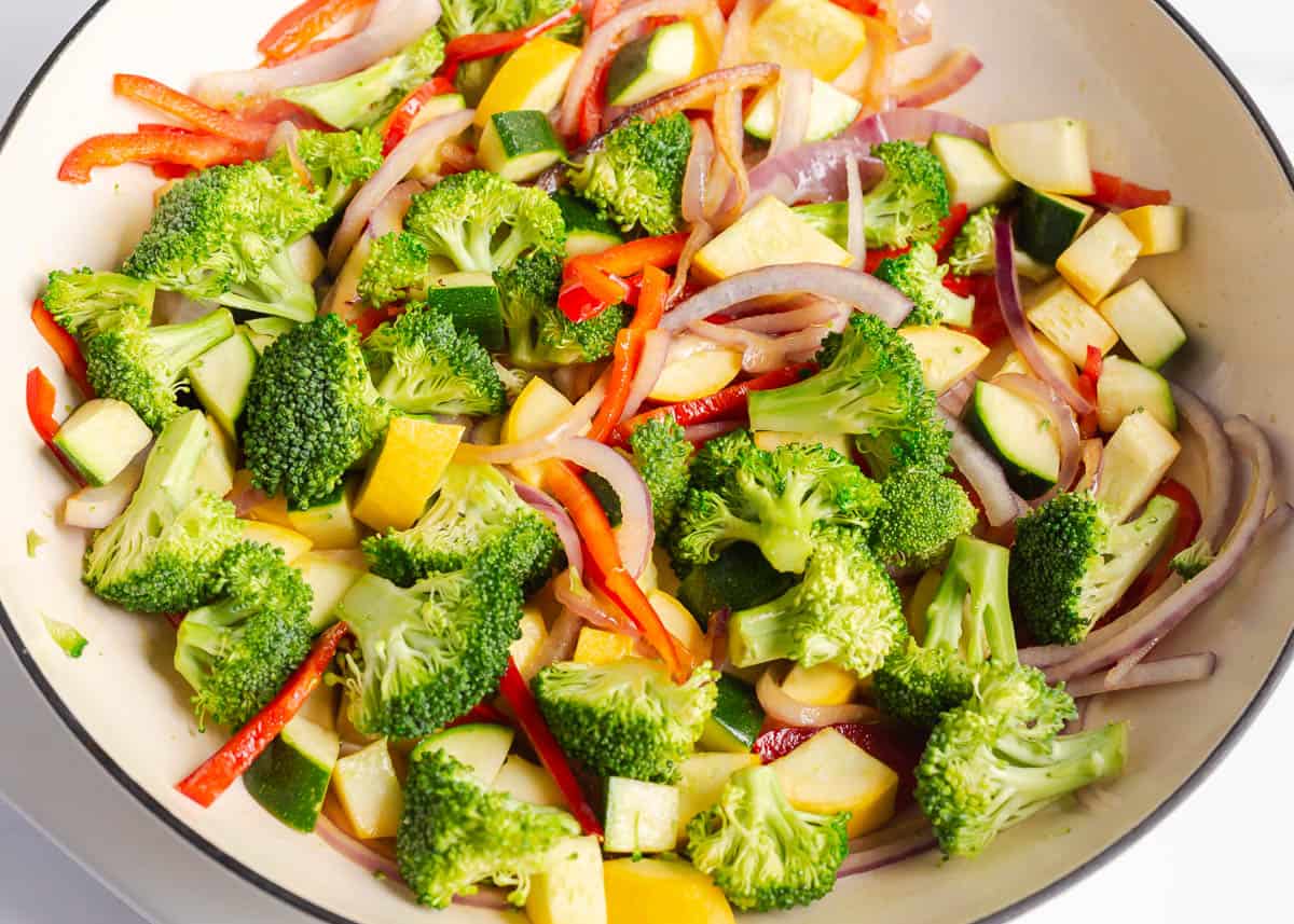 Showing sauteed vegetables for pasta primavera in a white skillet.