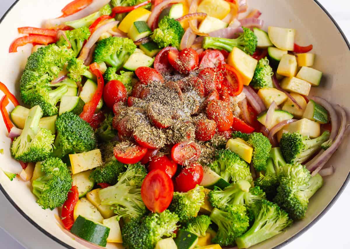 Pasta primavera vegetables with seasonings in a white skillet.