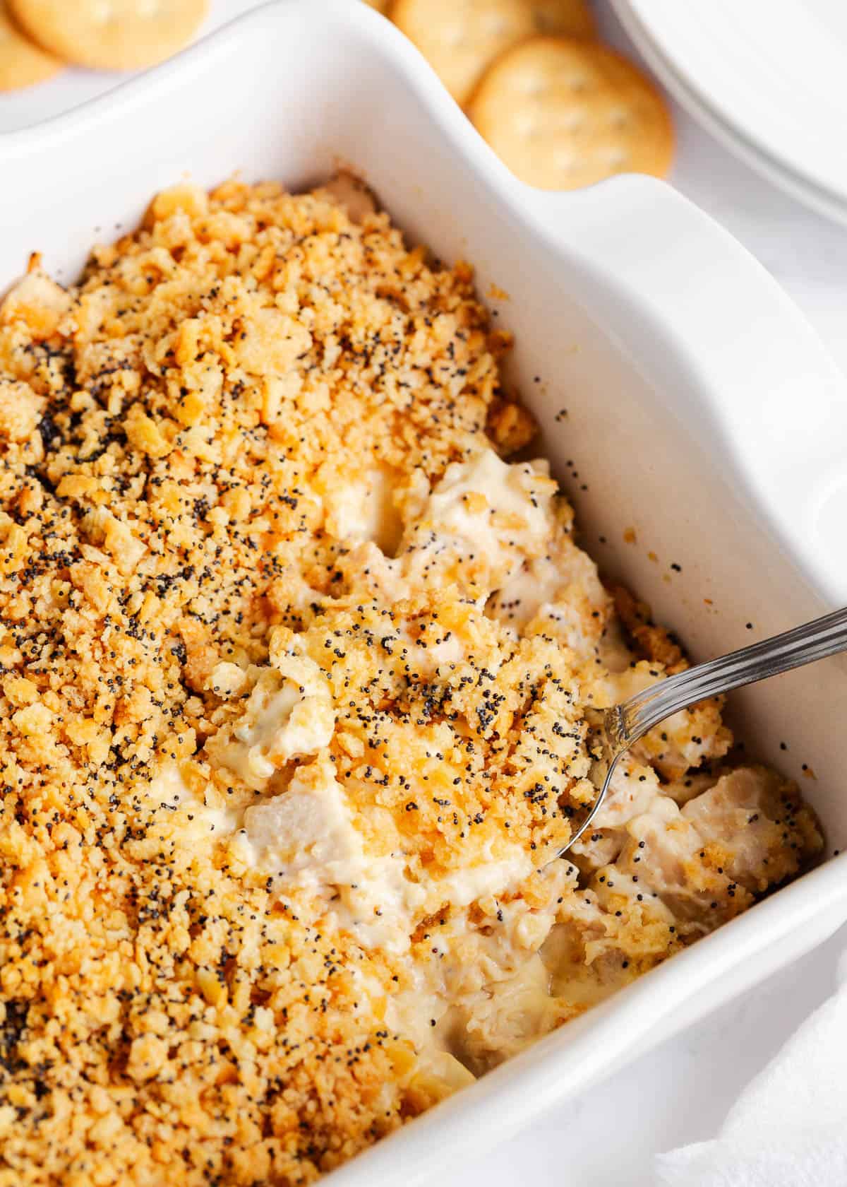 Poppy seed chicken casserole with serving spoon in white dish.