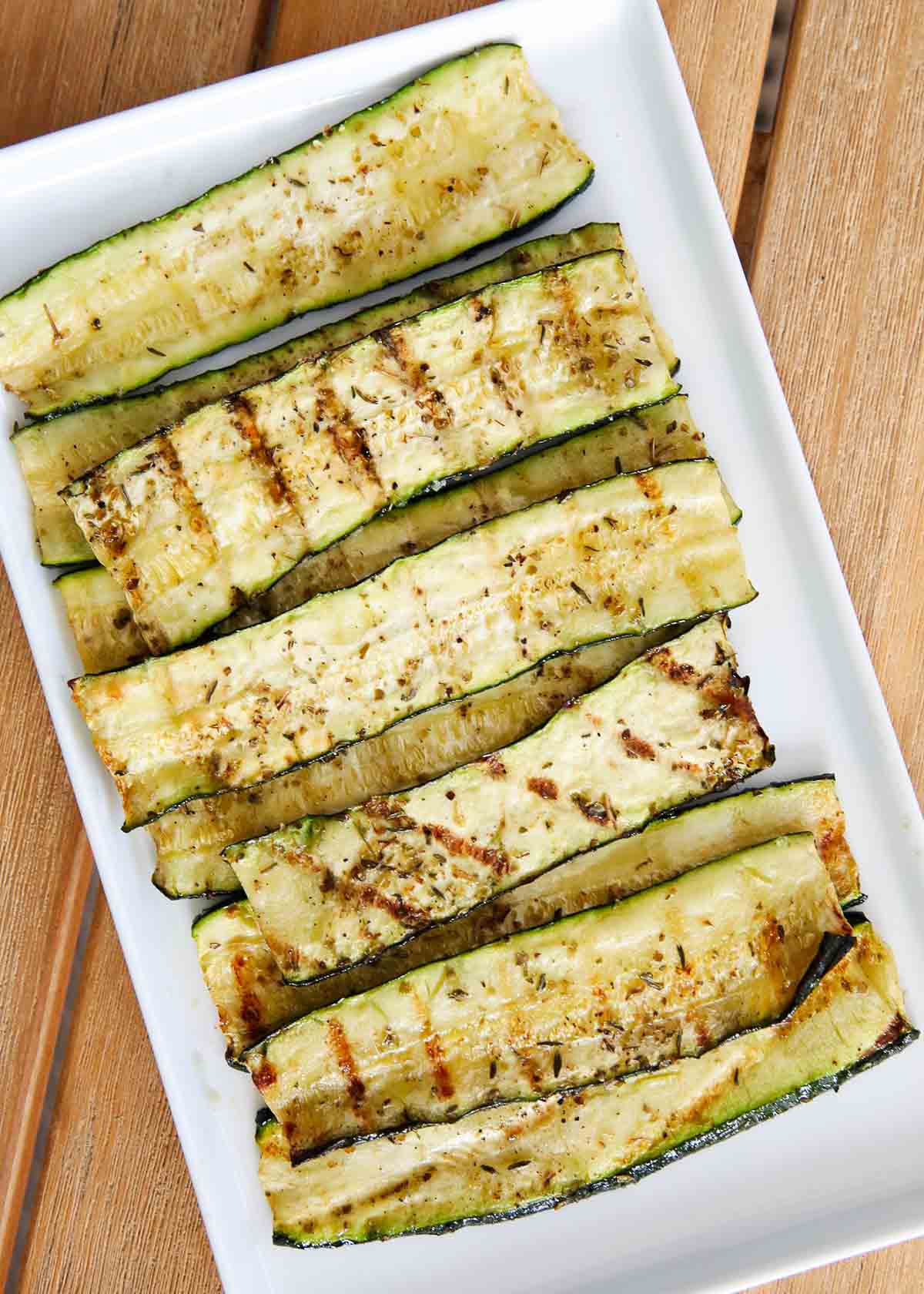 Grilled zucchini on a white plate on a wood table.