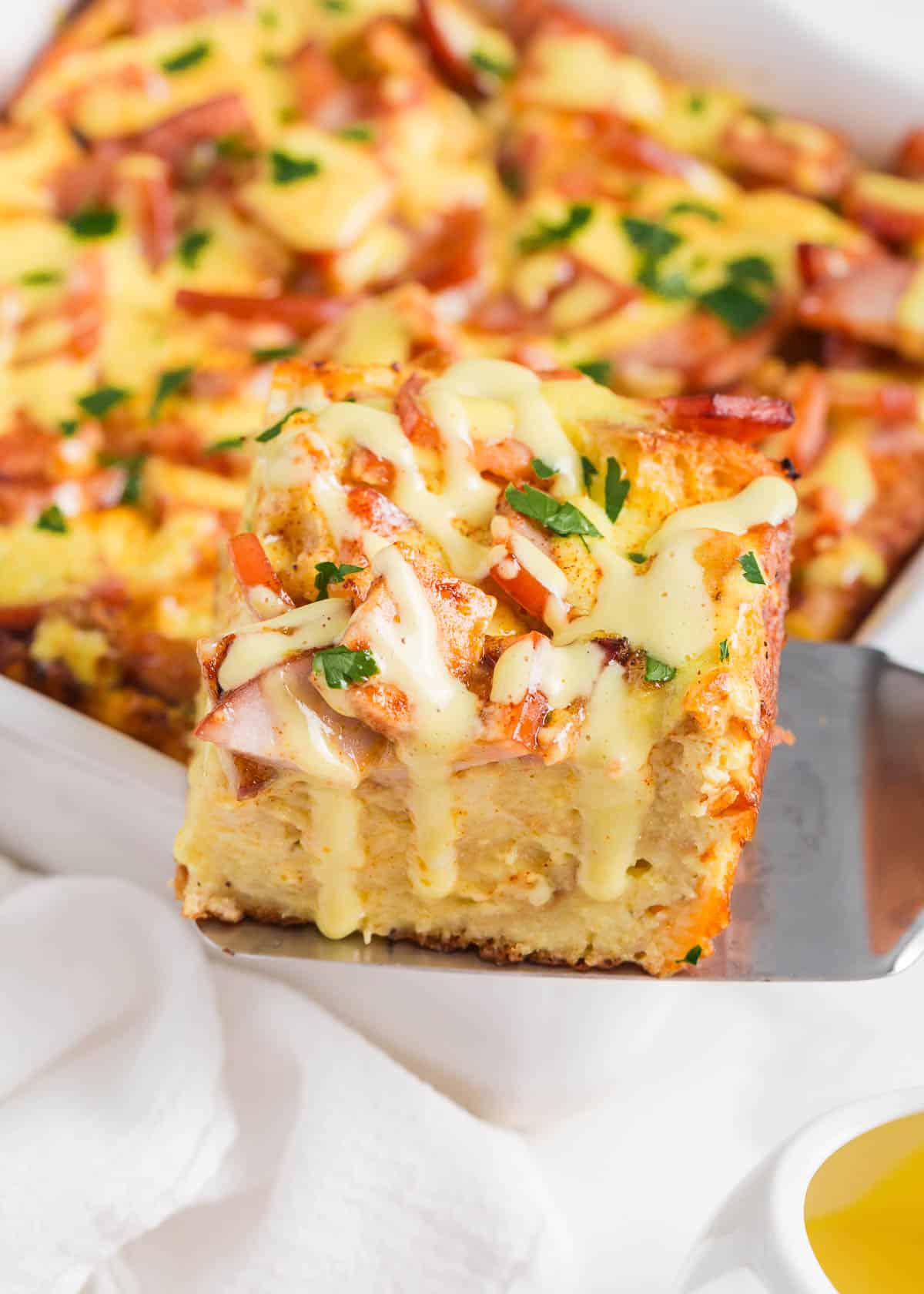 A slice of eggs benedict casserole being served on a spatula.