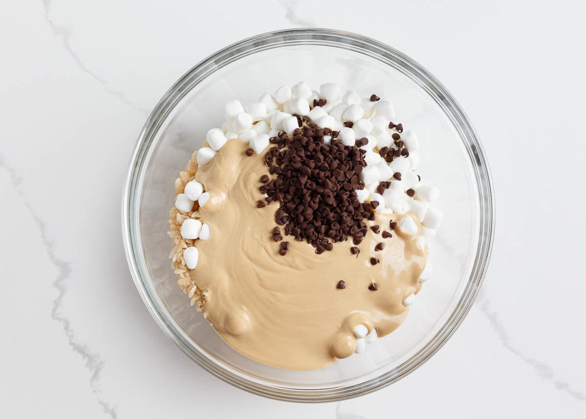 Melted peanut butter mixture with mini marshmallows, mini chocolate chips and rice krispies in a bowl.