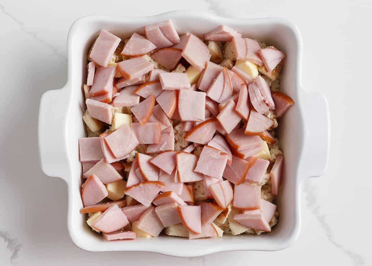 Canadian bacon and english muffins in a white baking dish.