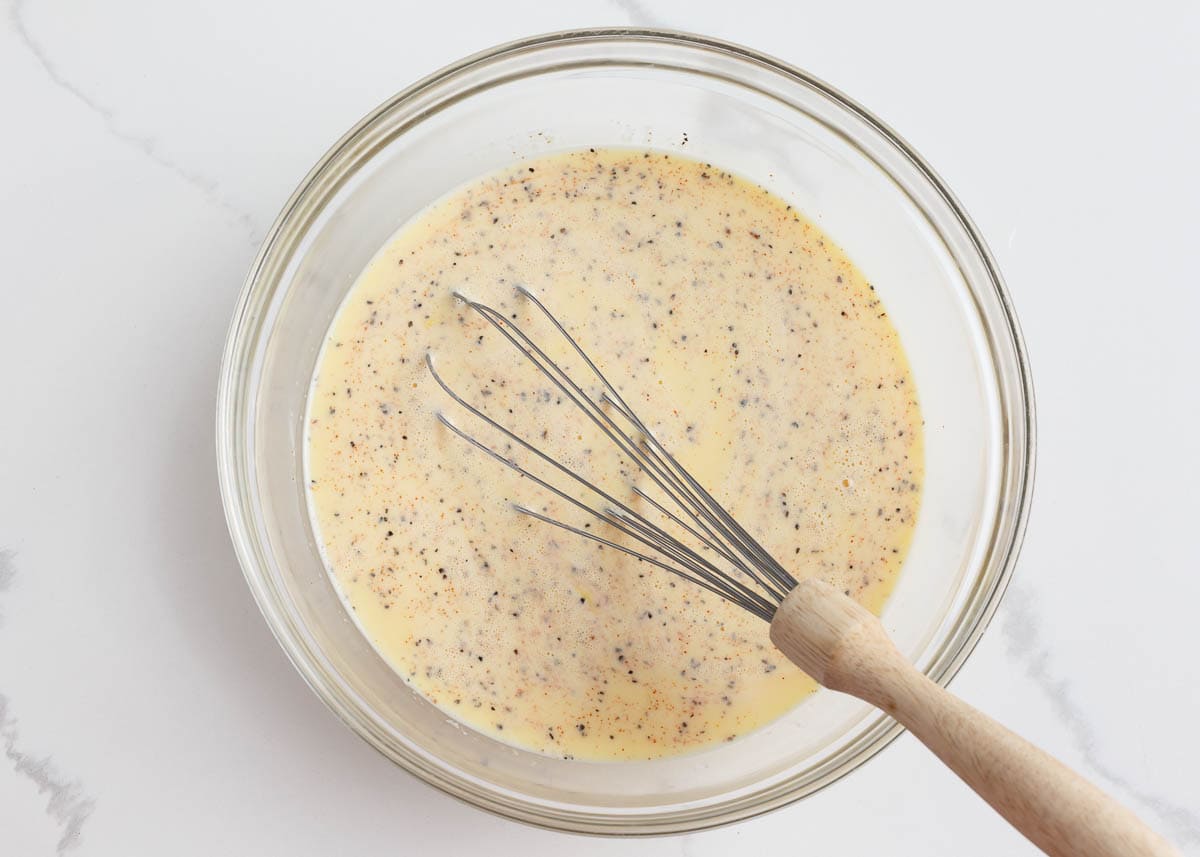 Milk, eggs and seasonings whisked in a glass bowl.