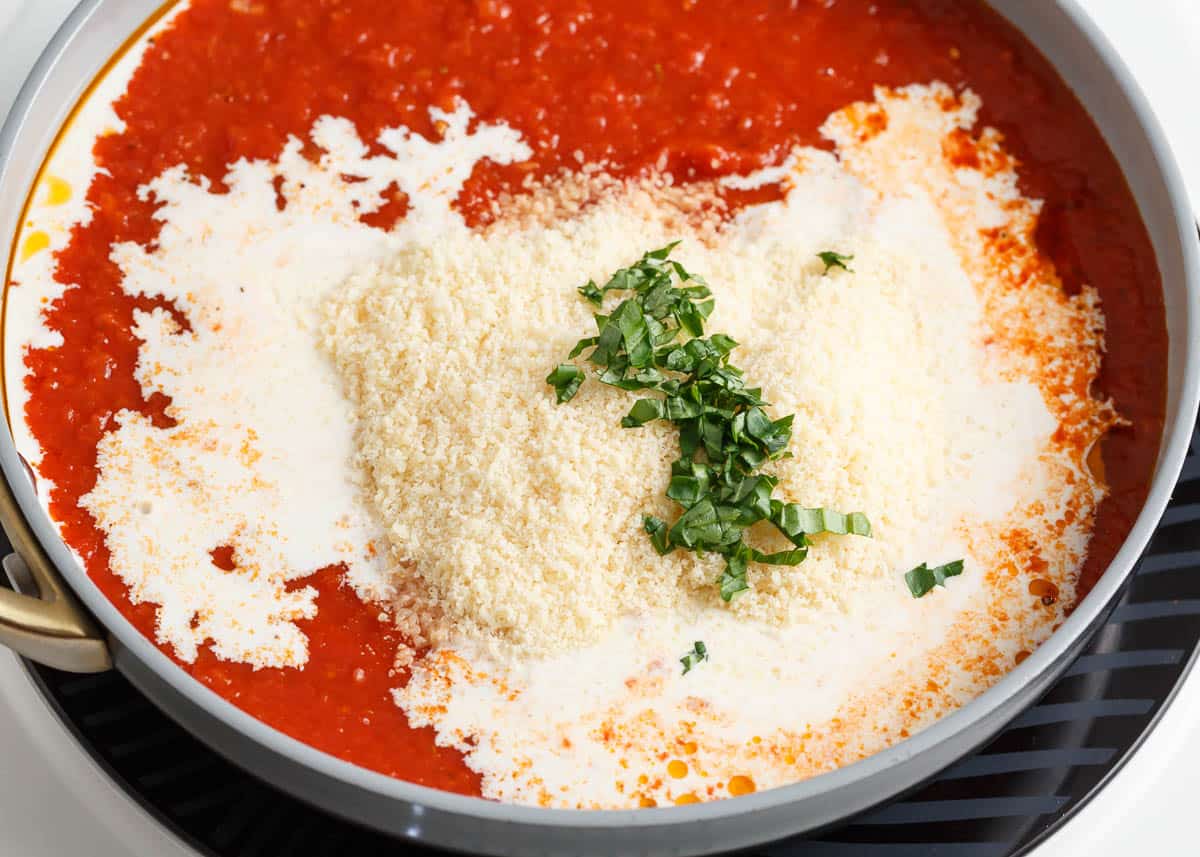 Cream and Parmesan added to tomatoes and seasonings in a skillet.