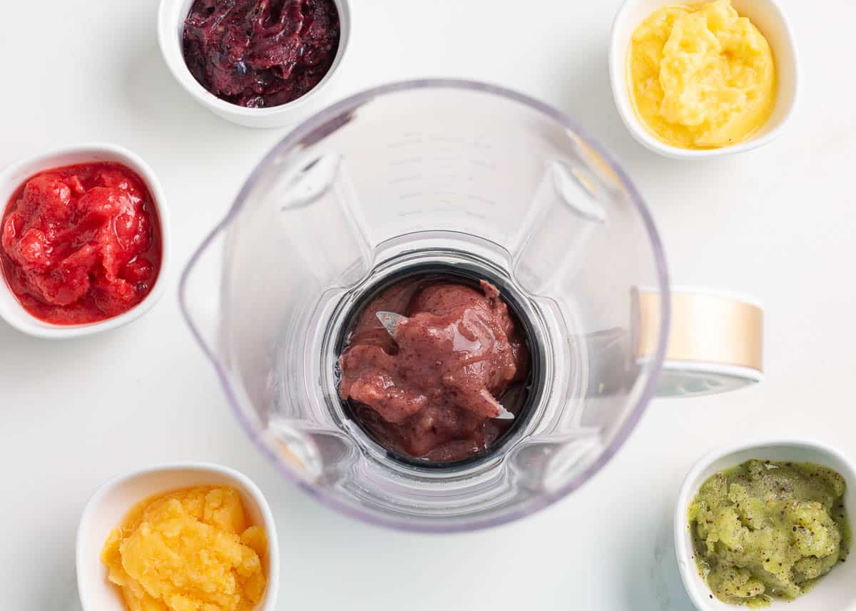 A blender with fruit puree and additional fruit purees on the counter. 