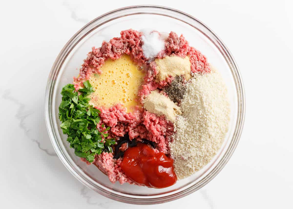 Ground beef, ketchup, panko breadcrumbs, parsley and egg in a bowl.