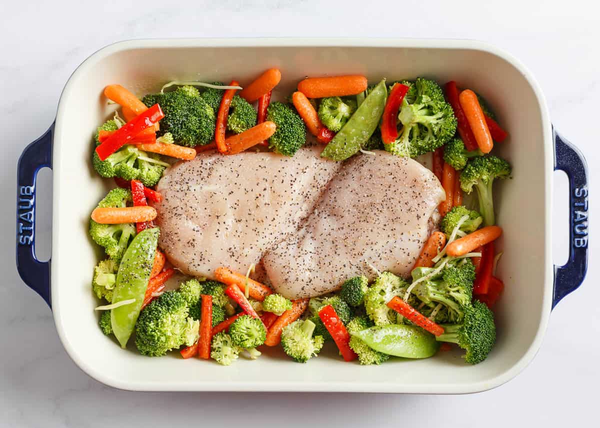 Unbaked chicken and vegetables in a white baking dish.