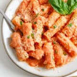 Pink sauce pasta in a large bowl with basil and Parmesan garnish.