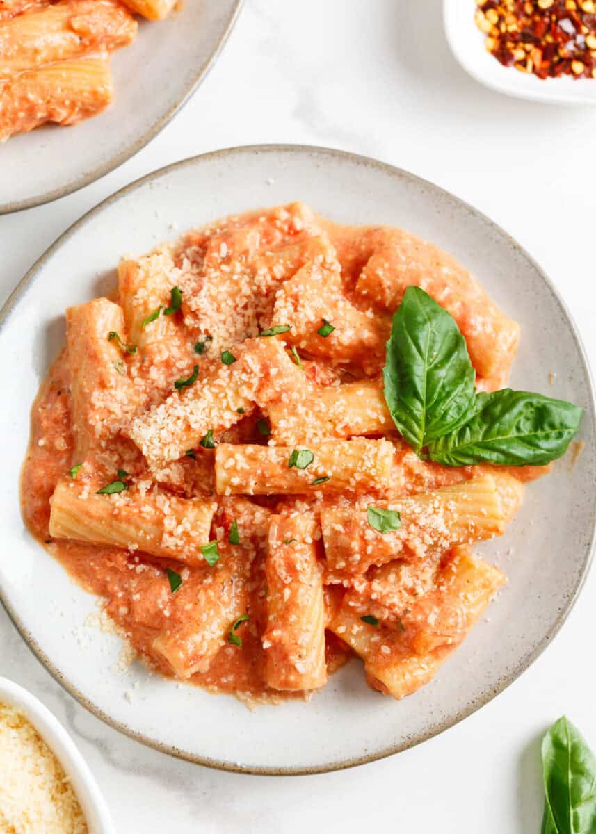 Pasta with pink sauce on a plate with Parmesan and basil garnish.