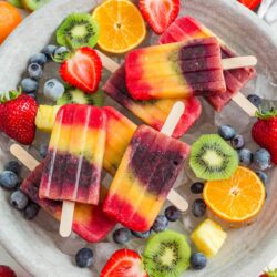 A tray with rainbow popsicles and fresh fruit.