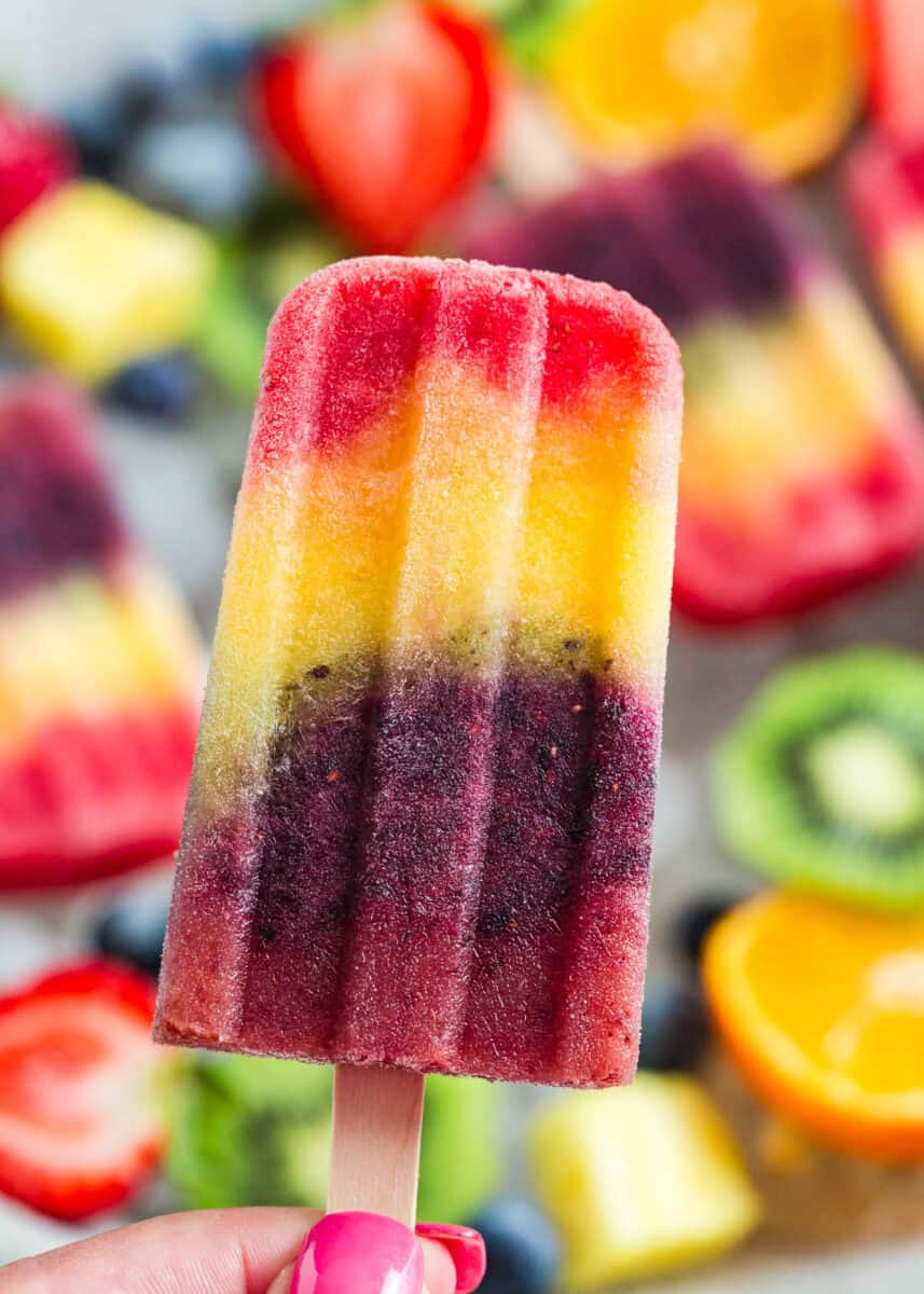 A hand holding a rainbow popsicle.