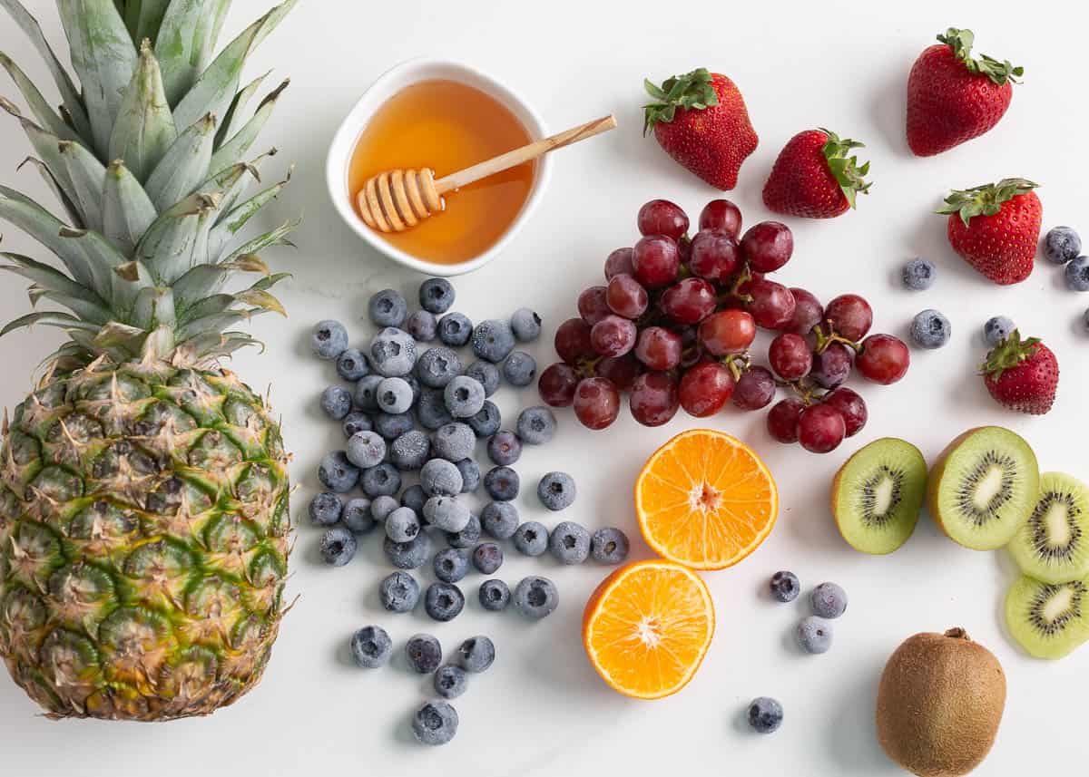 Pineapple, grapes, kiwi, strawberries and oranges with honey on the counter.