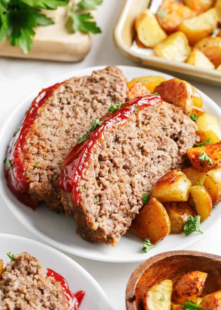 Two slices of sheet pan meatloaf with potatoes on a white plate.