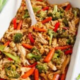 Teriyaki chicken casserole in a white baking dish with serving spoon.