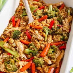 Teriyaki chicken casserole in a white baking dish with serving spoon.