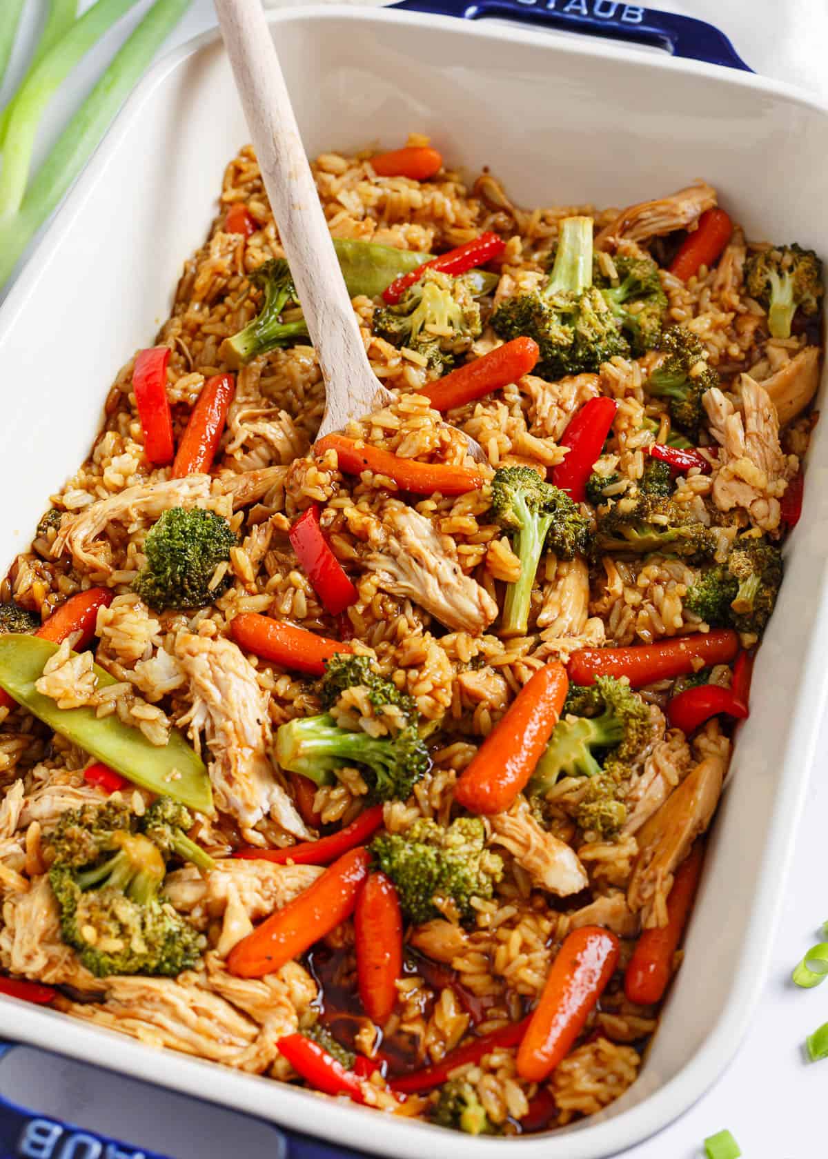 Teriyaki chicken casserole in a white baking dish with serving spoon.