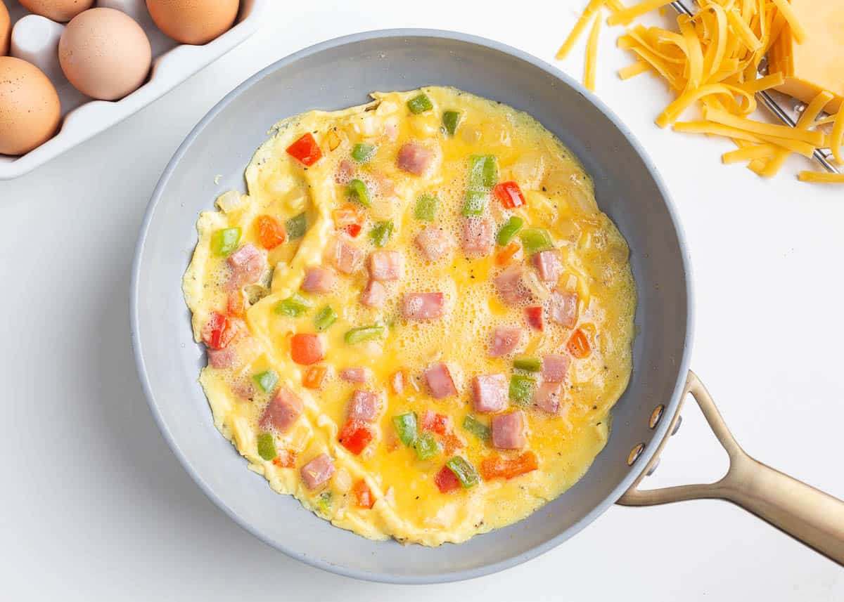 Showing how to make a western omelette in a skillet.