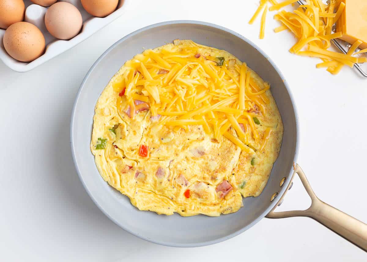 Showing how to make a western omelette with cheese in a skillet.