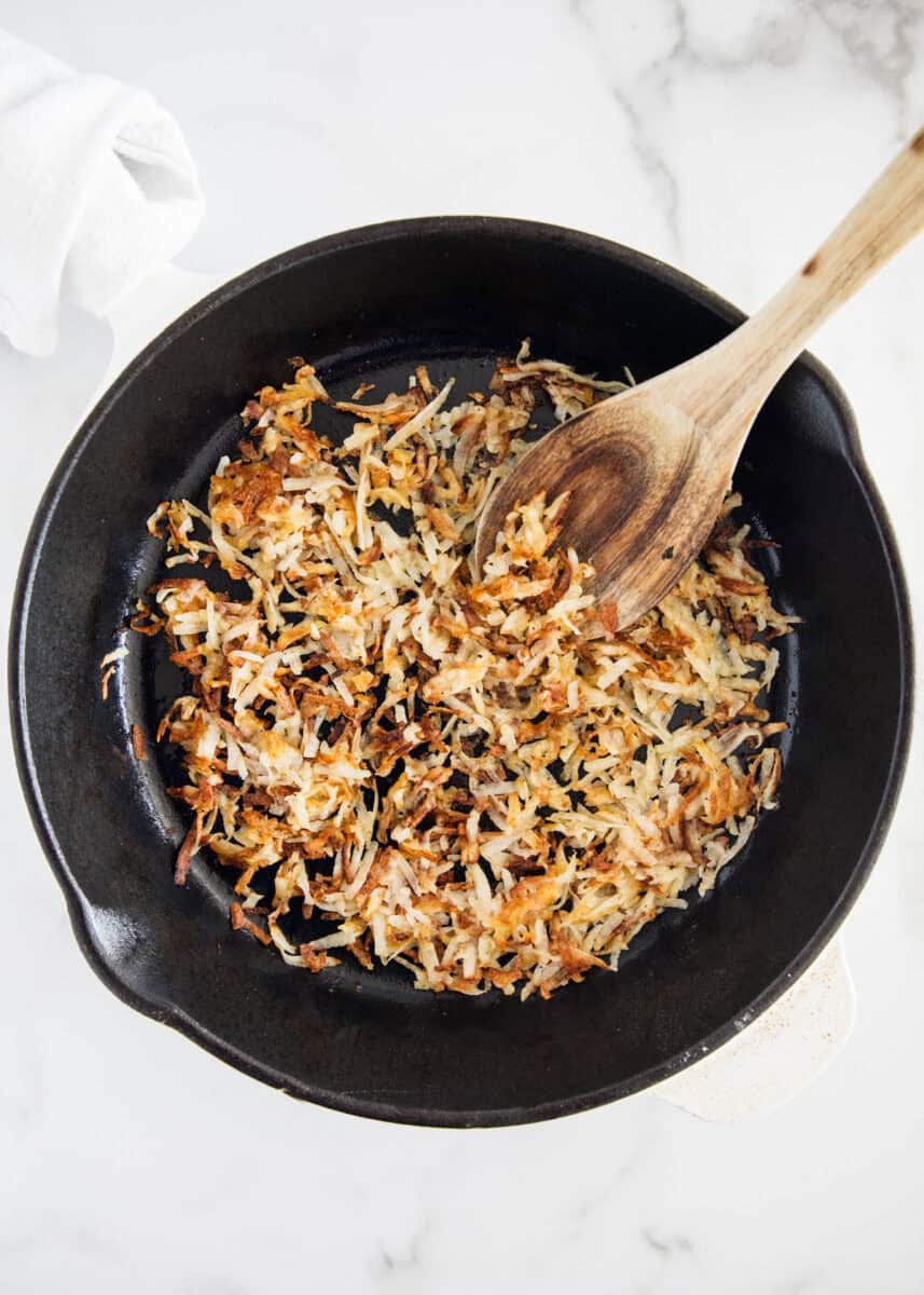 Cooking hash browns in a skillet with a wooden spoon.