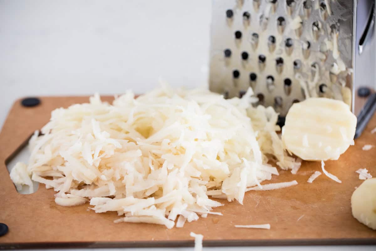 Shredded potatoes and cheese grater on a cutting board.