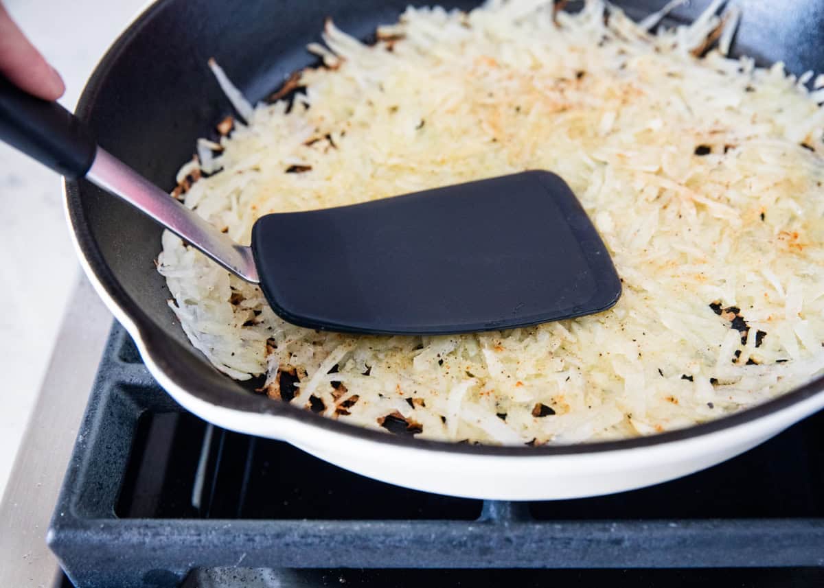 Pressing shredded hash brown potatoes with a spatula in a skillet.