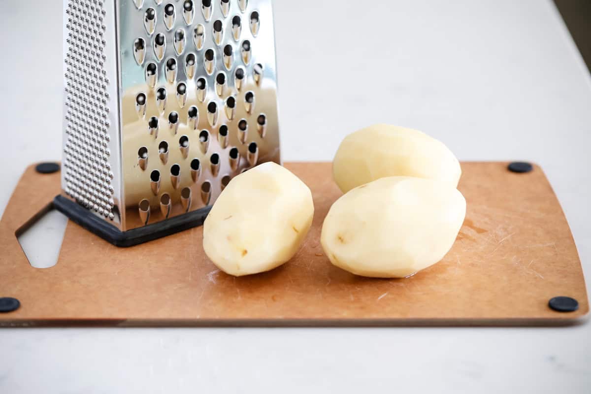 Potatoes on a cutting board with a cheese grater.