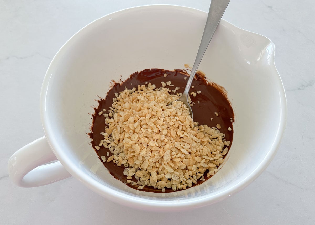 Stirring rice crisp cereal into melted chocolate in a white bowl.