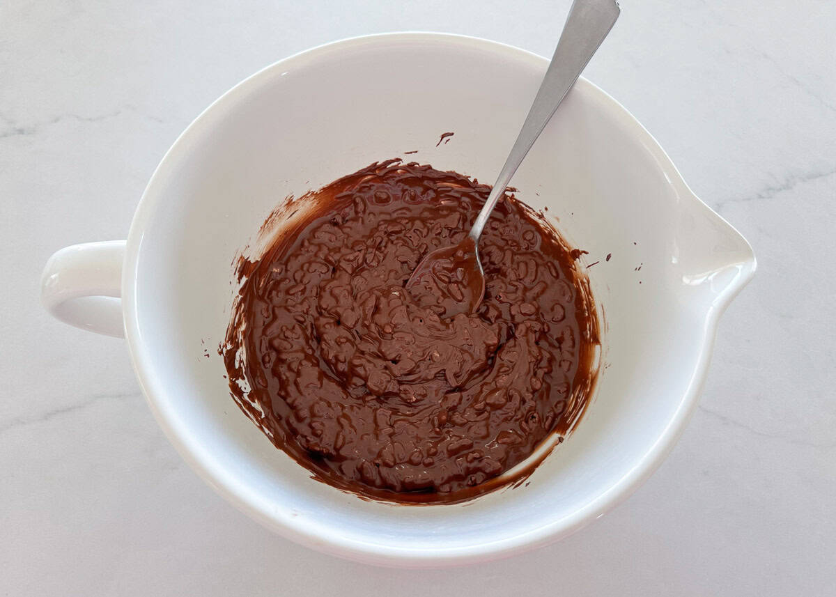 White bowl with melted chocolate and rice krispies cereal stirred together. 