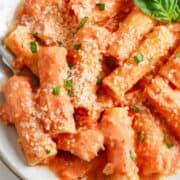 Pink sauce pasta on a white plate with basil garnish.