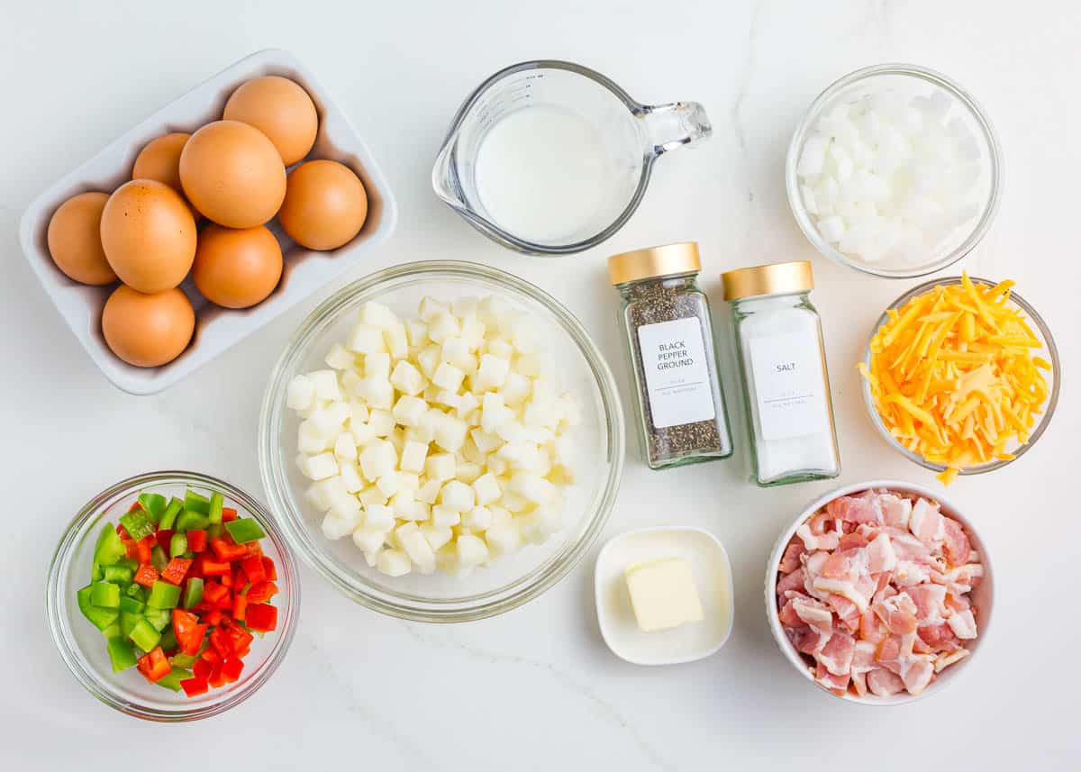 Eggs, frozen diced potatoes, bacon, bell peppers, milk, cheese and seasonings on counter.