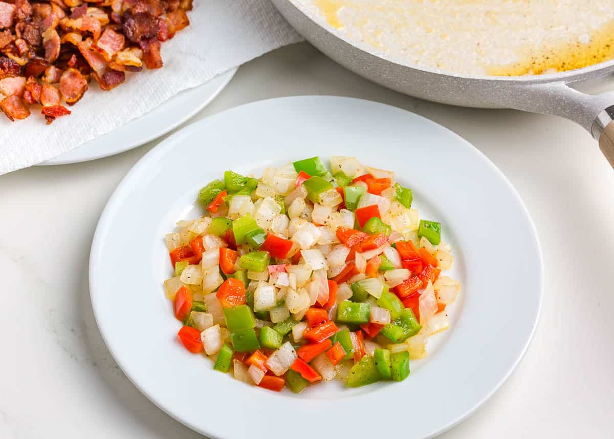 Sauteed peppers on a plate and cooked chopped bacon on a plate.