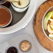 Caramel apple bar with sauces in crockpot, apples in a bowl and a tray of toppings.