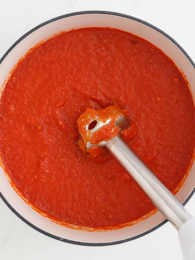 Using an immersion blender to blend tomato sauce.