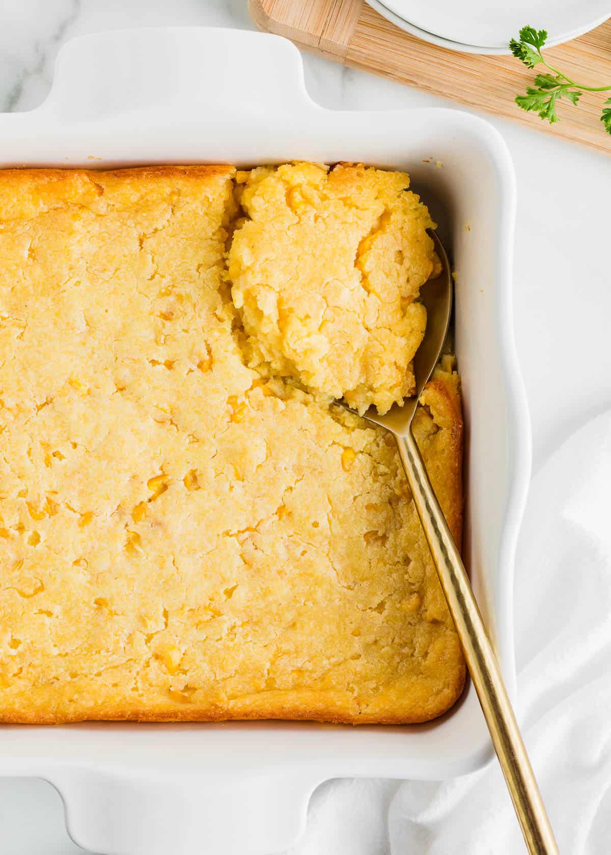 Jiffy corn pudding in white pan with spoon.