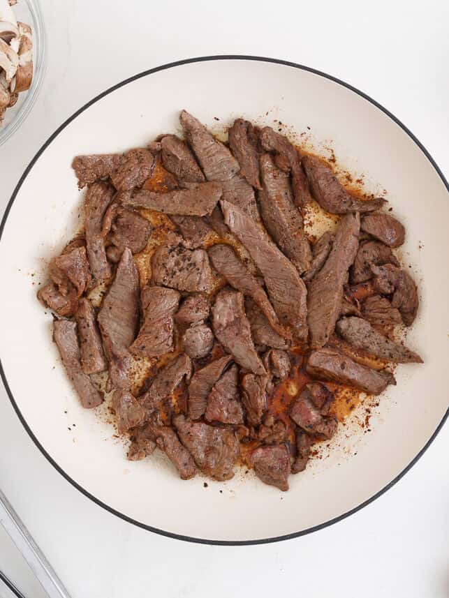 Strips of beef for stroganoff seared in a skillet.